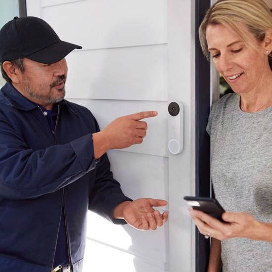 Delivery man pointing at Google Nest Doorbell with household owner showing him what it looks like on the phone 